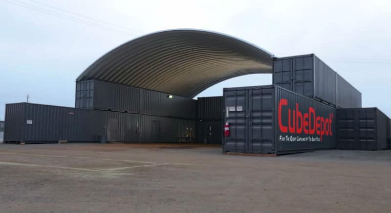 large structure with steel arch roof mounted on several stacked gray shipping containers with a cube depot logo