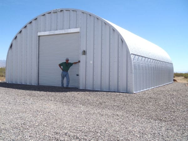 steel quonset hut with roll up metal garage door and man standing in front