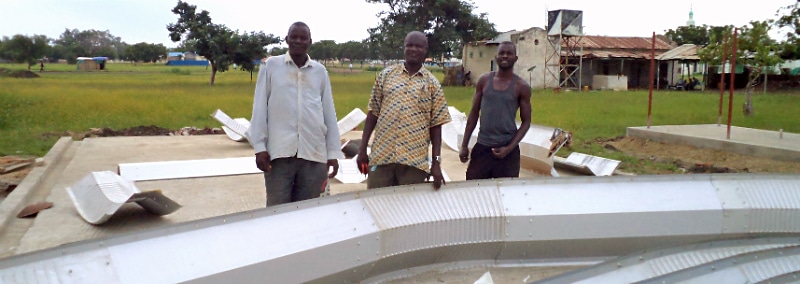 three men standing in front of quonset hut arch on the ground