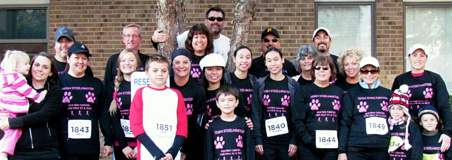 Group of people smiling wearing matching black and pink shirts and marathon bibs