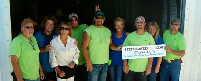 group of people smiling in front of quonset hut holding steelmaster building sign