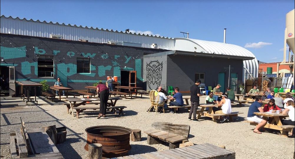 people sitting at picnic tables in front of brewery building with quonset hut at the end