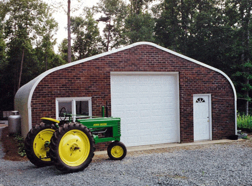 Steel Quonset Hut barn with brick endwalls and green tractor in front of it.