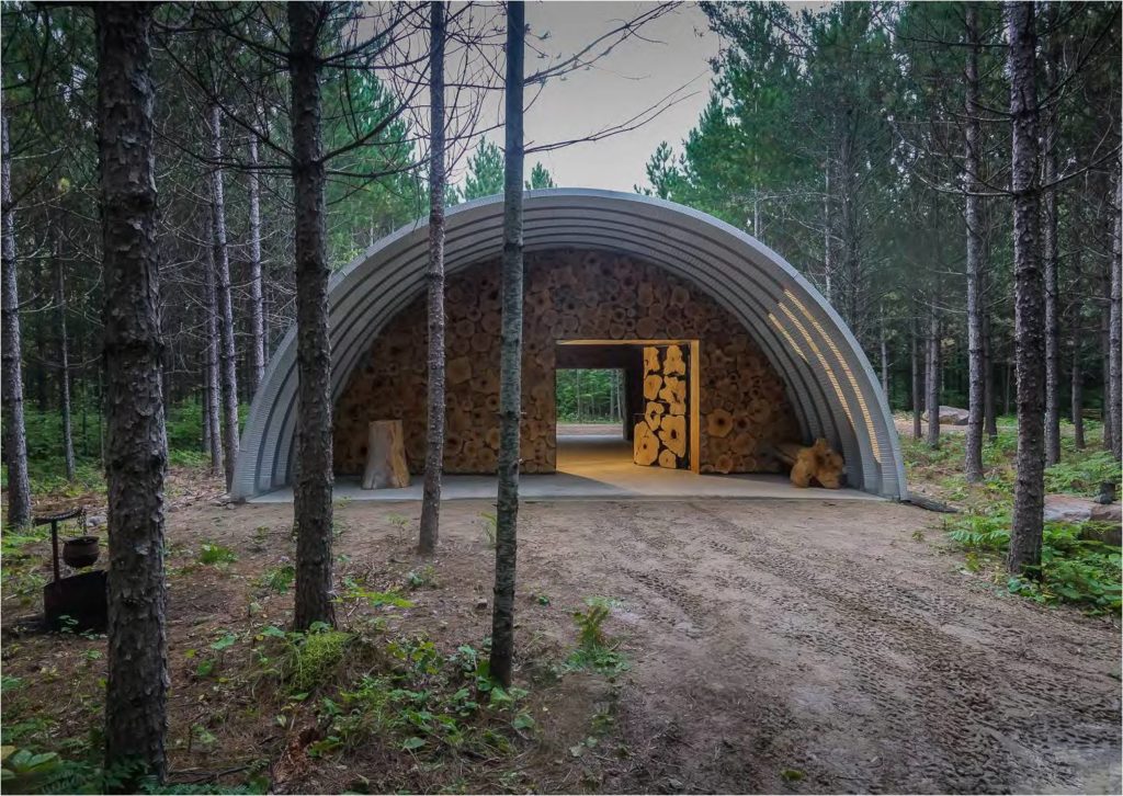 q-model quonset hut in the forest with arch overhang and custom endwall made from logs