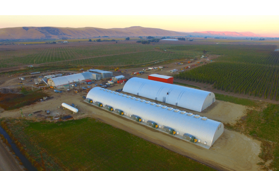 two large quonset huts on farm land with sunset in background