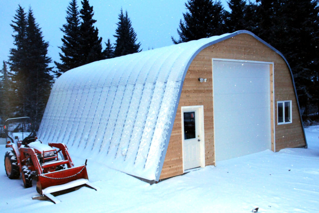 X-Model steel workshop with a custom wood front end wall, white entry door and white garage door covered in snow