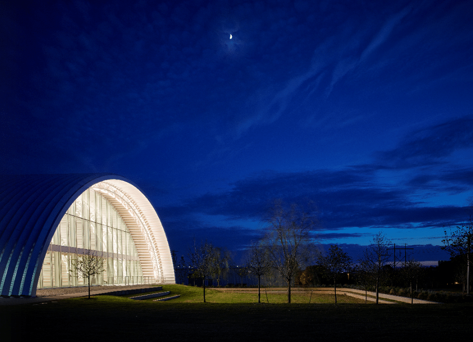 steel arch building large floor to ceiling glass windows under moonlight grass entrance