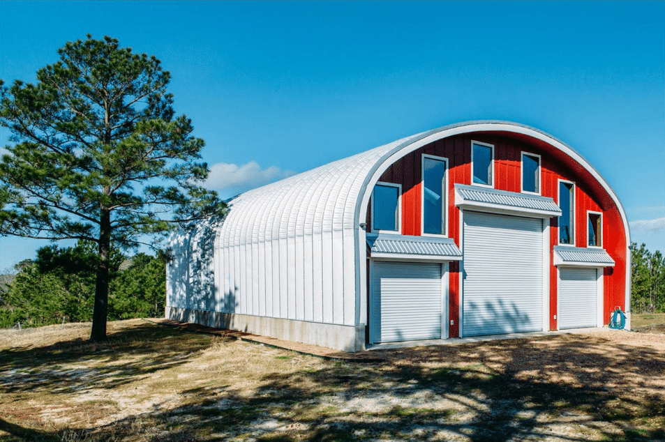 large steel quonset barn with red endwalls, three garage doors and windows of multiple sizes