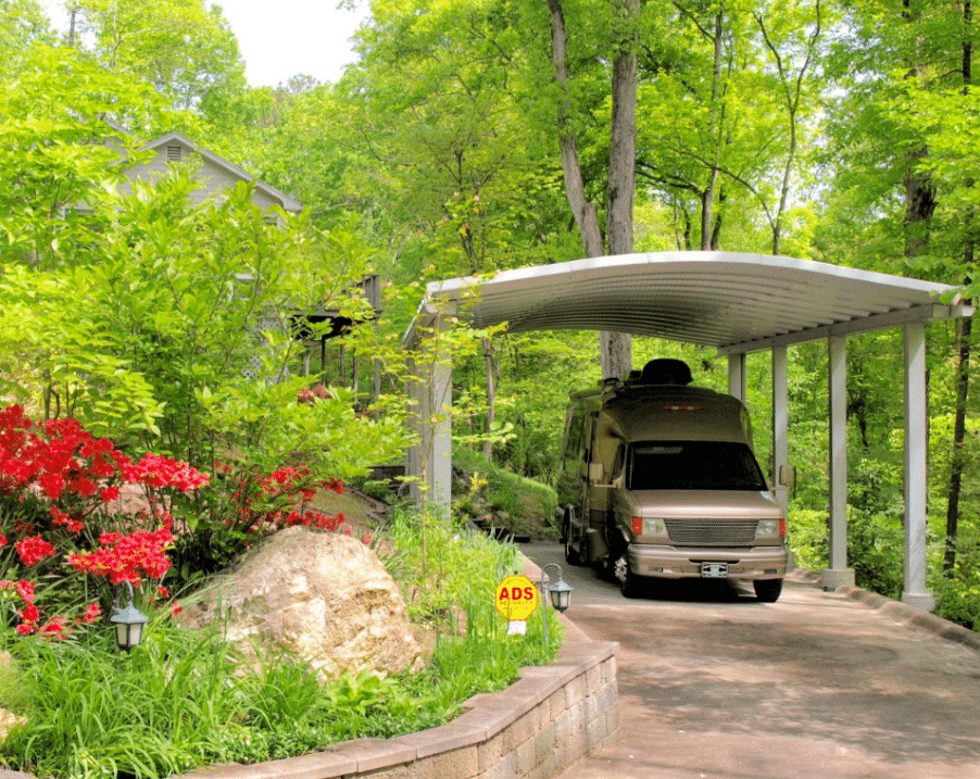 carport with rv parked underneath surrounded by trees and flowers