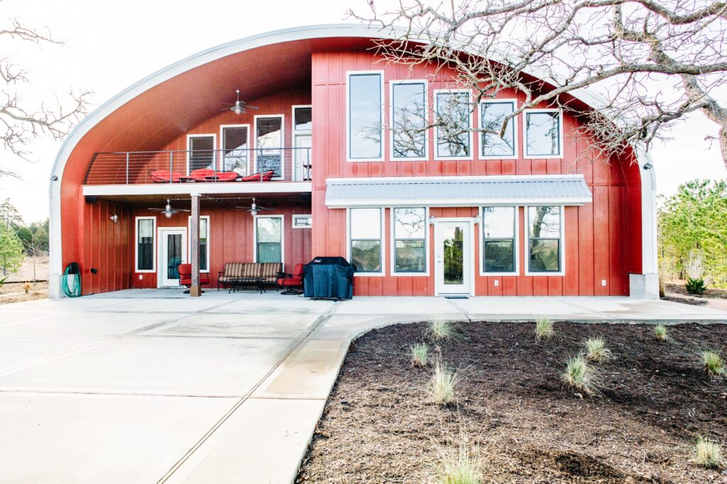 Steel arch house multiple glass windows covered grill concrete driveway outdoor seating awning