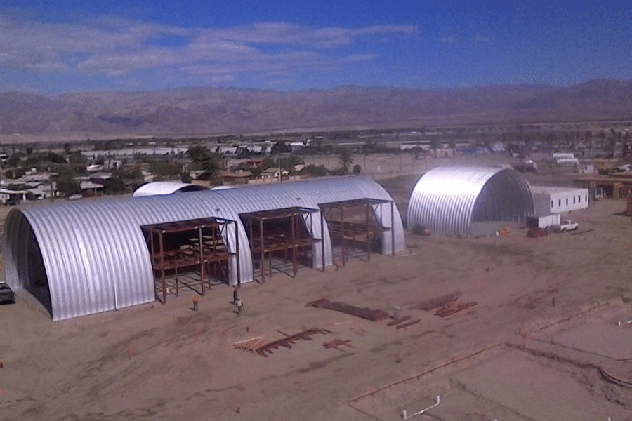 multiple steel arch buildings construction workers working on steel support beam structure in desert