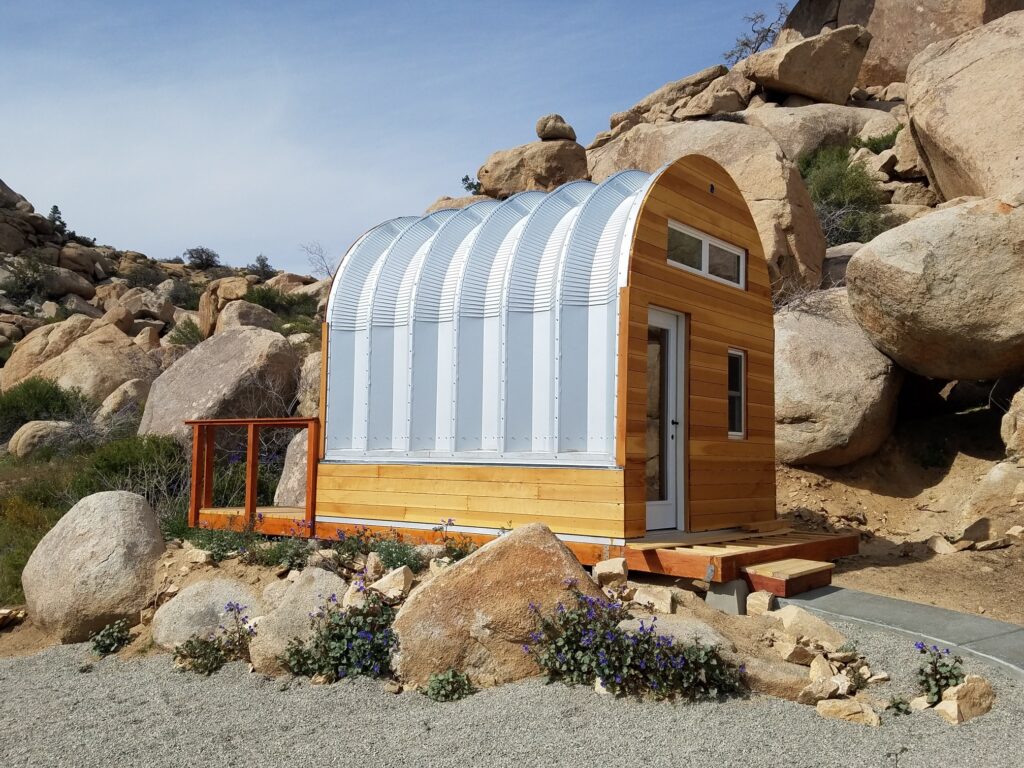 mini quonset hut cabin light wood with glass windows black sliding doors rough terrain boulders small porch