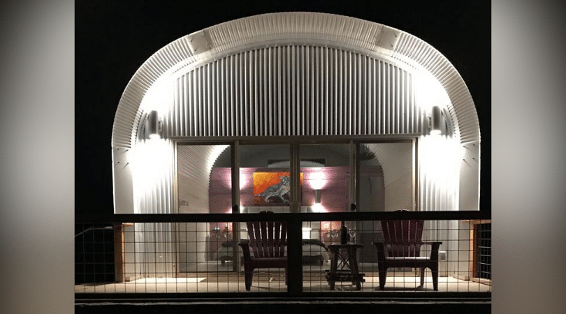 steel arch house front porch wood railing two chairs glass sliding doors purple wall with art bed inside house