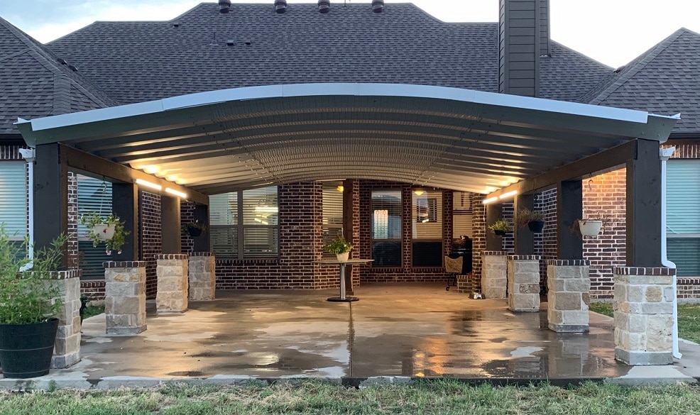 A carport with stone posts and a steel corrugated roof outside a brick home