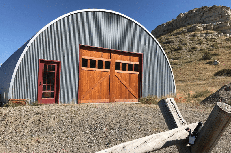 q-model steel quonset hut with steel cladding endwall, two wooden doors and red entry door with mountain landscape in the background