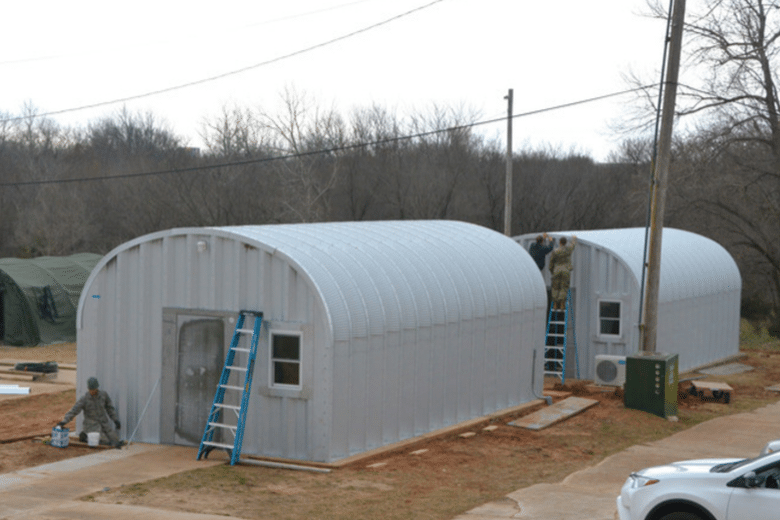 two steel arch buildings multiple military members on ladders working on buildings green tent