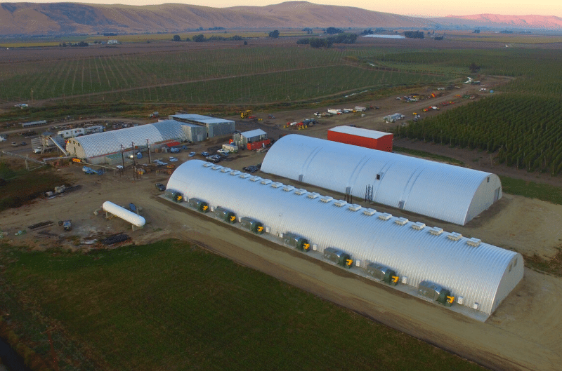 Four steel arch buildings with multiple air conditioner units attached fields behind structures red barn