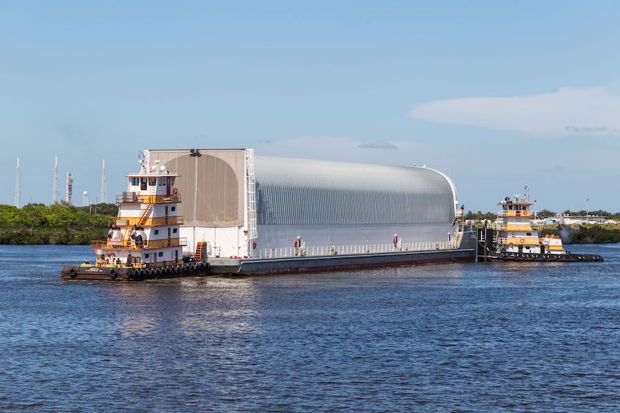 steel arch barge pushed by two white and yellow tug boats in water
