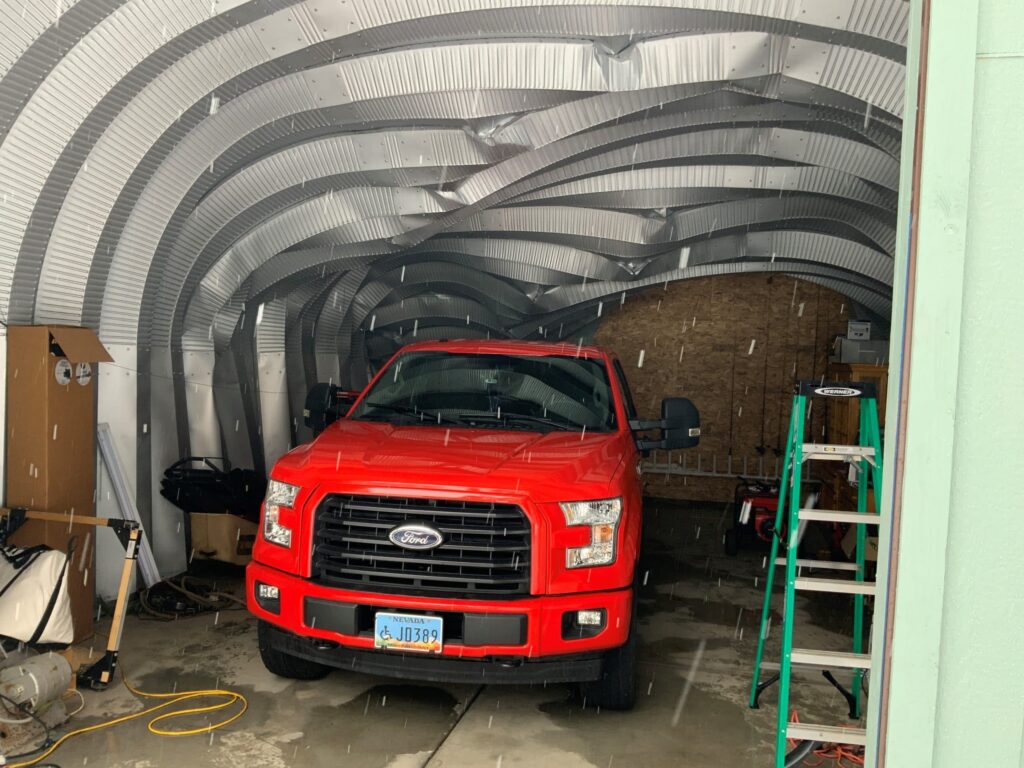 fallen tree on steel building inside view red truck parked inside falling tree damage to steel building arch style steel garage with fallen tree interior view ladder inside