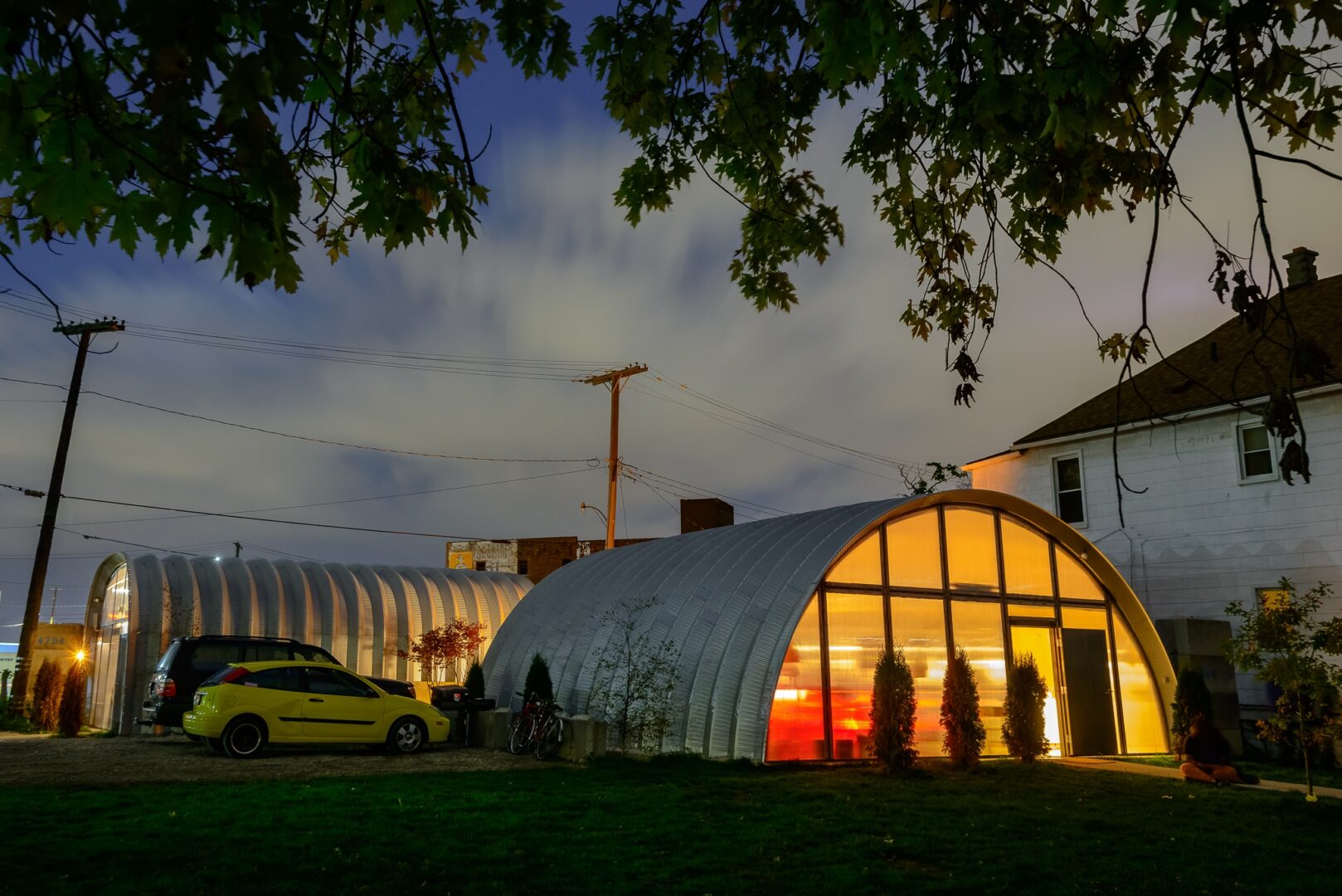 two cars parked outside steel building yellow car by steel building steel building with lights on during the night trees by steel building side by side steel buildings arch style