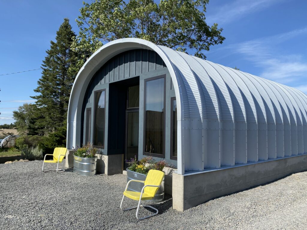 Steel hut with great front and multiple glass windows with two yellow chairs surrounded by gravel