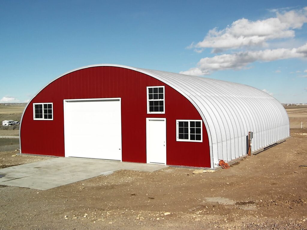 Quonset Hut red end wall white garage door concrete slab grass field in background blue skies