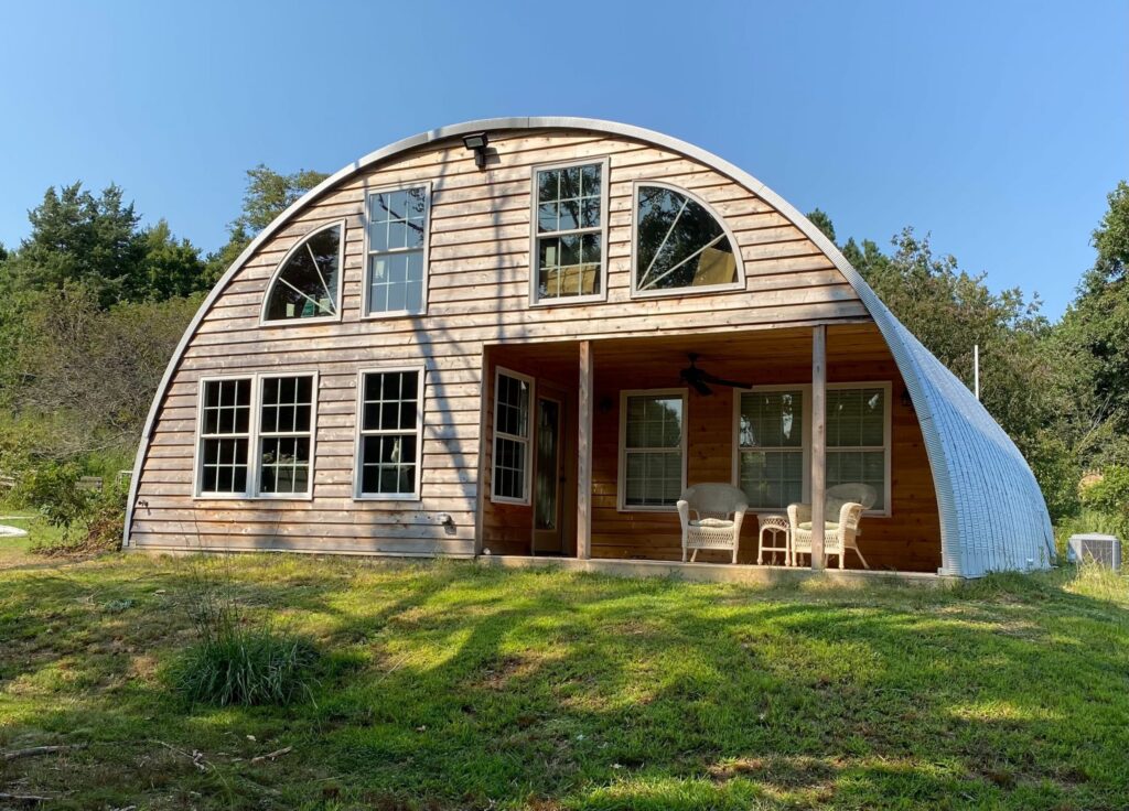 Custom Quonset Hut home with custom wooden endwall filled with windows and a front porch
