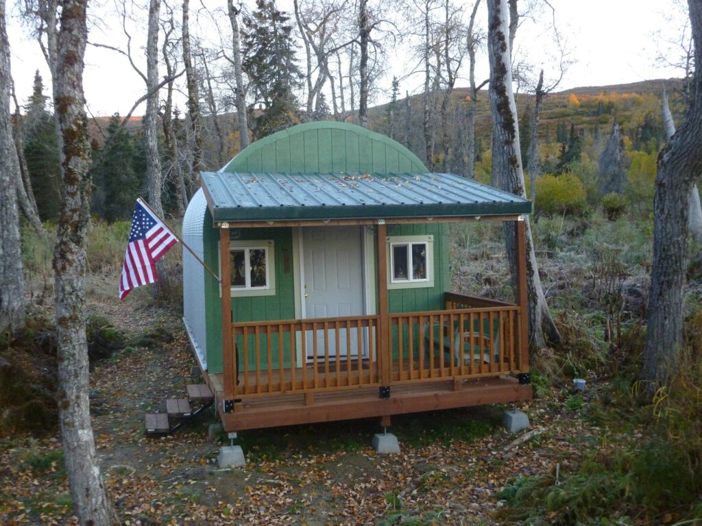 S model Quonset hut with custom green endwall with man door and windows and wooden awning and front porch connected to the front