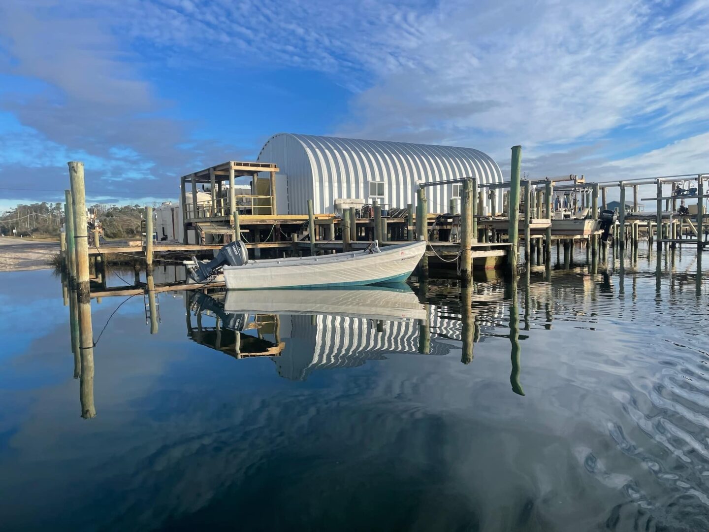 Quonset hut shellfish hatchery on wooden docks above water, small boat tied to end of the dock