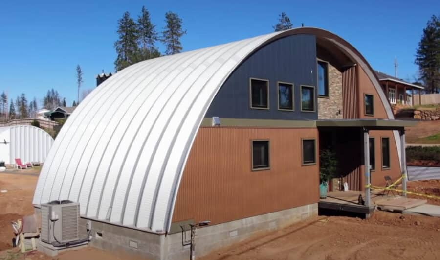 Quonset home with blue, orange, and stone custom endwall, awning over front porch and entrance, white quonset hut structure in the backyard
