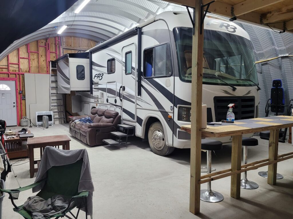 Inside Quonset RV shed with RV inside, wooden bar and stools, recliner couch