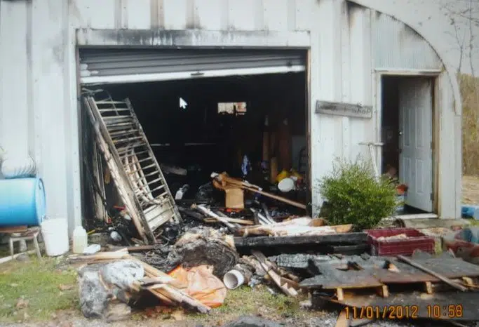 Quonset structure with some soot, burnt objects strewn in and around workshop, open rolling and entrance door.