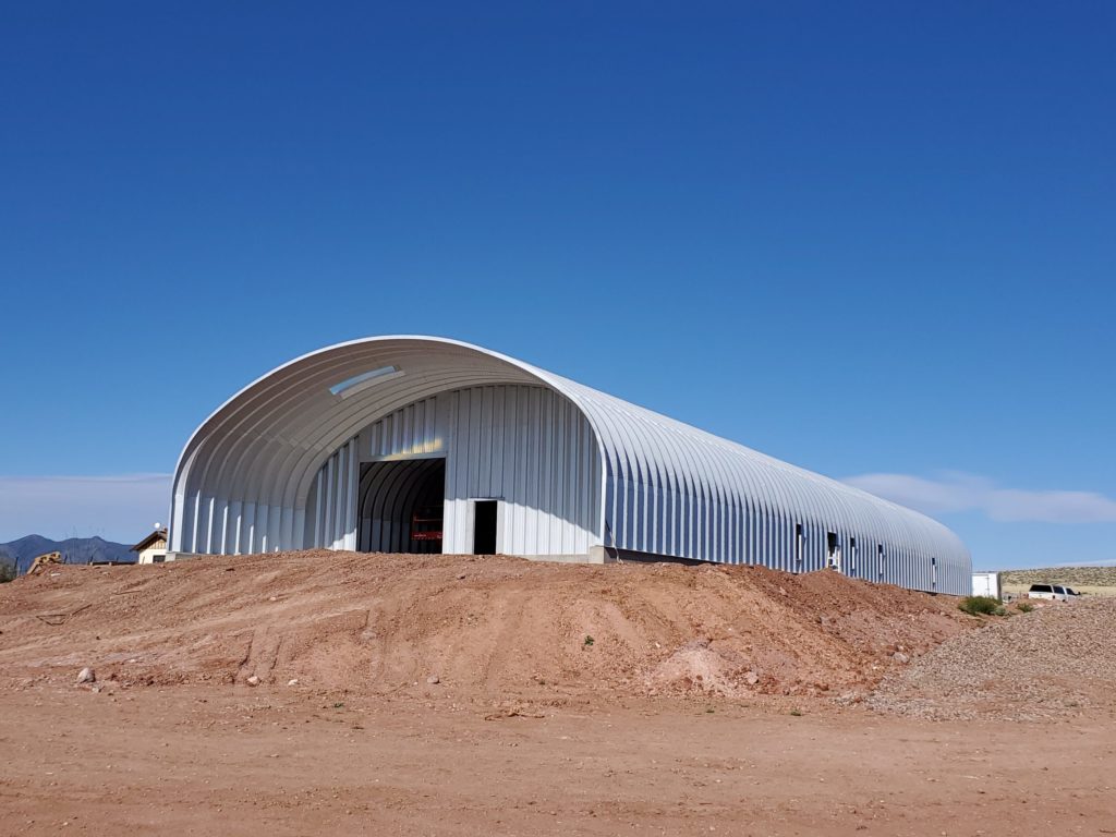Industrial sized S-model Quonset with large awning with skylight over entrance, steel endwalls with rolling door and front entrance.