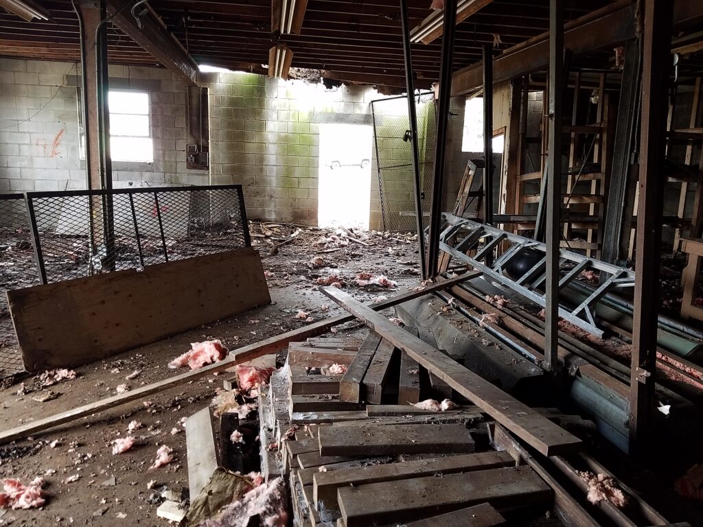 Inside crumbling abandoned building, dirt, trash, insulation, and wooden planks on ground