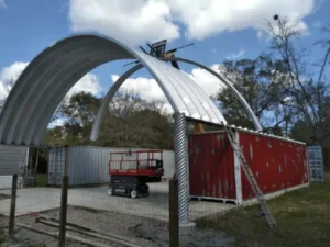 Construction of container cover, white and red freight containers, large yellow lift, latter leaning on side on container