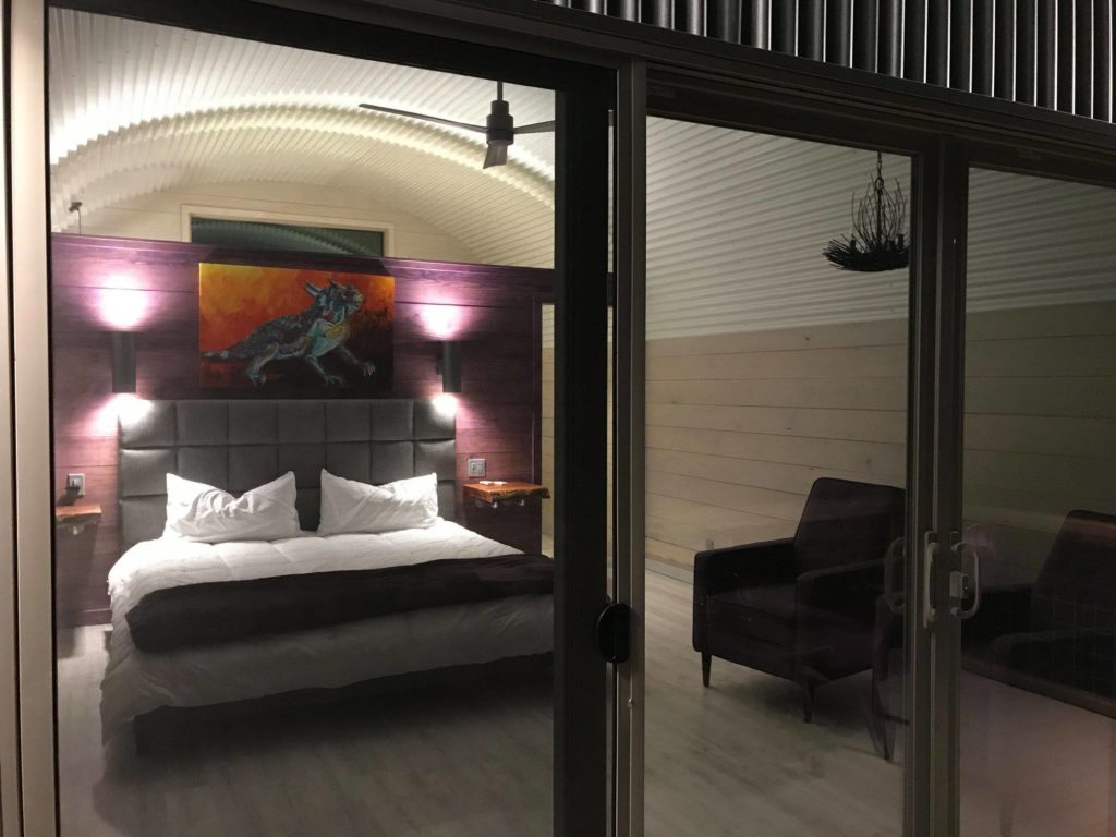 Inside a Quonset casita: bedroom, wooden and ribbed covered walls, wood panel flooring.