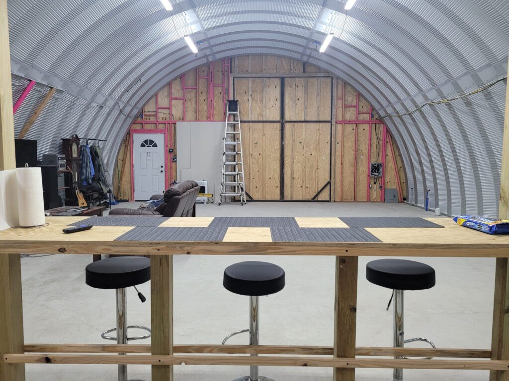 Inside of Quonset RV shed, wooden endwall, wooden bar with stools, tv and couch