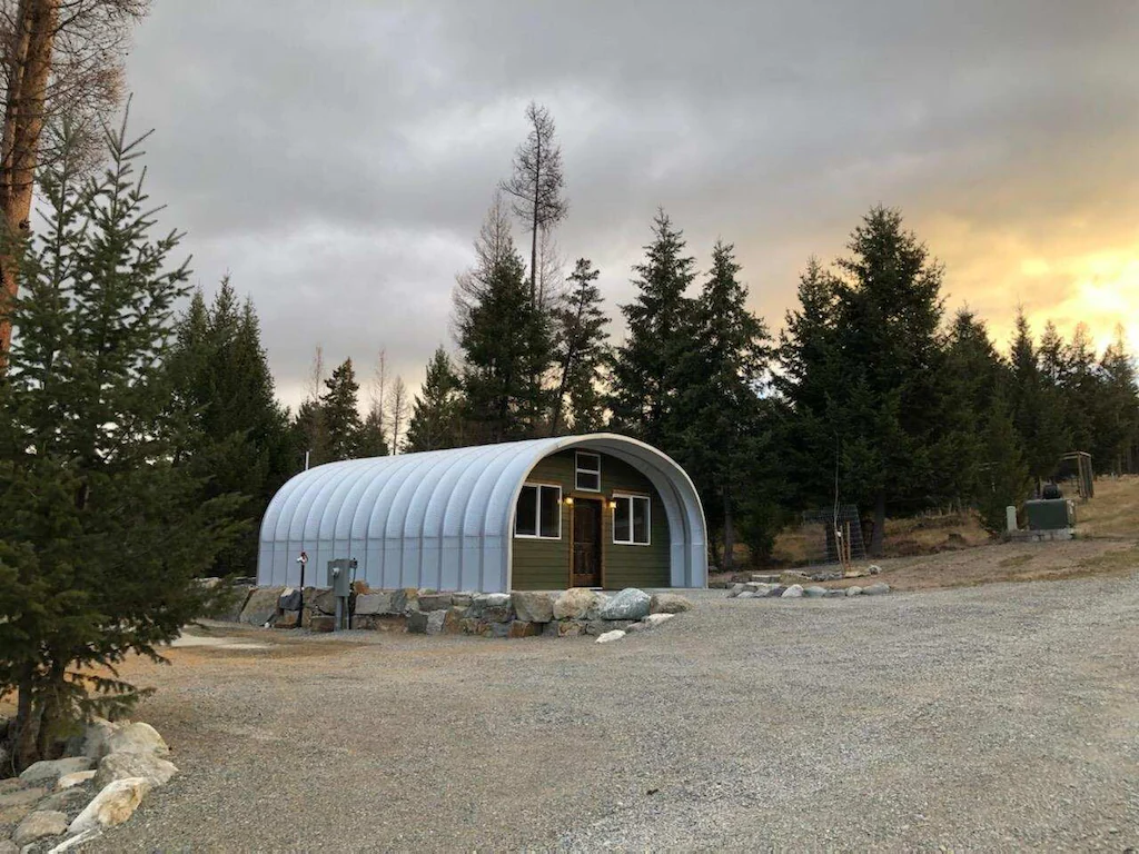 S-model quonset structure with recessed green custom endwall, pine trees and sunset background
