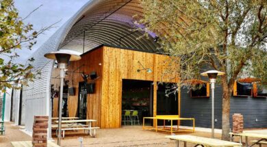 A curved steel roofing system covering a wooden building with picnic tables underneath