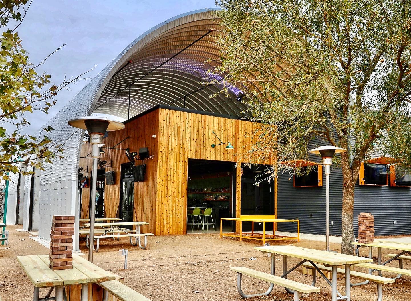 A curved steel roofing system covering a wooden building with picnic tables underneath