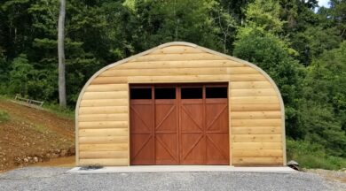 A-Model Quonset hut with custom wood end wall, dark brown garage door, and trees in the background.