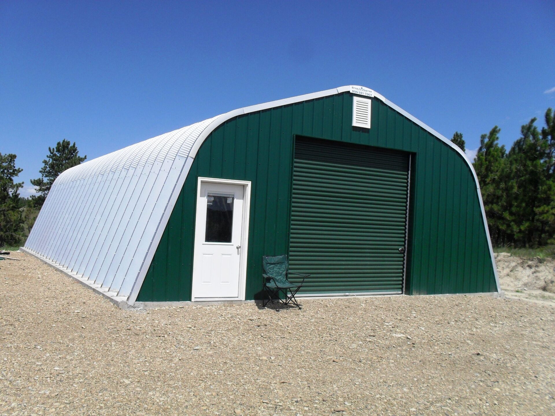 Steel Quonset workshop with dark green front end wall, white entry door, and green garage door