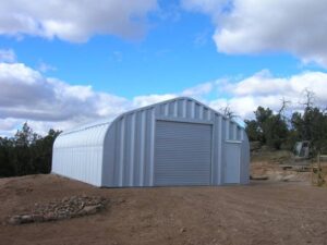 A-Model Quonset hut with steel end wall, steel garage door, steel man door, and a circle of rocks in front.