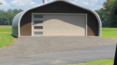 A-Model Quonset hut with custom brown end wall, large tan garage door with four horizontal windows, and a rotating ventilation system on top.