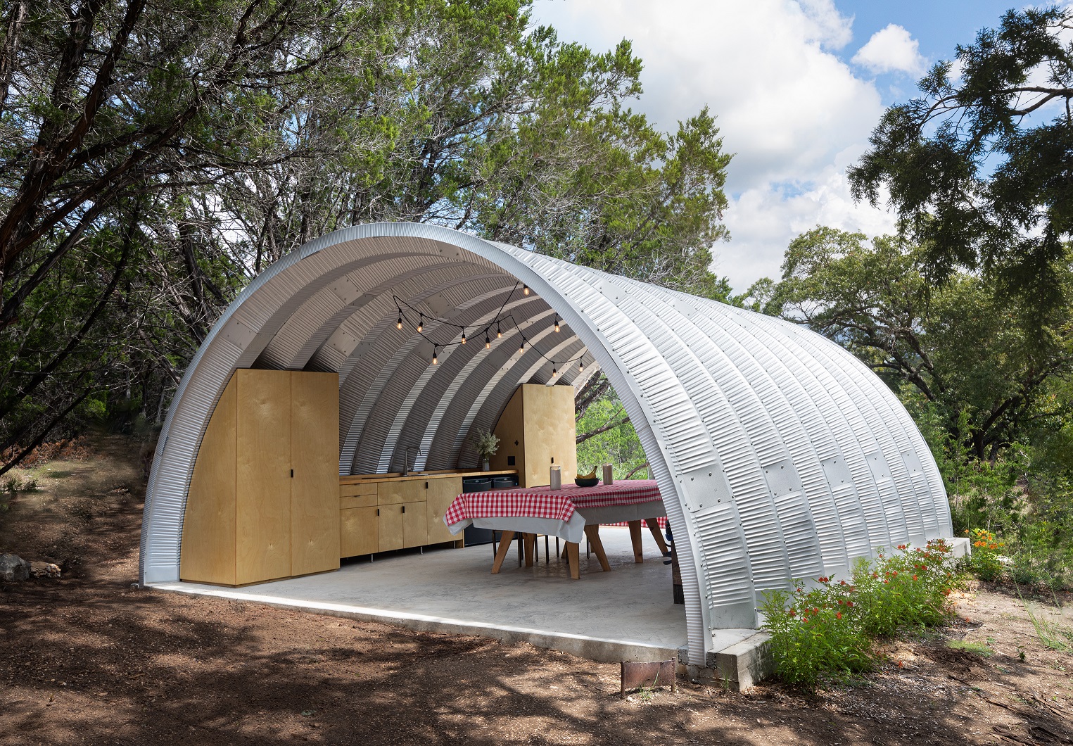 Open ended Q-Model Quonset hut covering a picnic table with a checkered table cloth and a row of custom cabinets