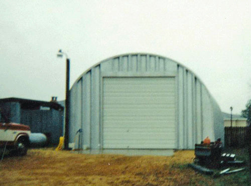 Vintage picture of an S-Model Quonset hut with steel end wall, white garage door, and a vintage red and white truck on the left.