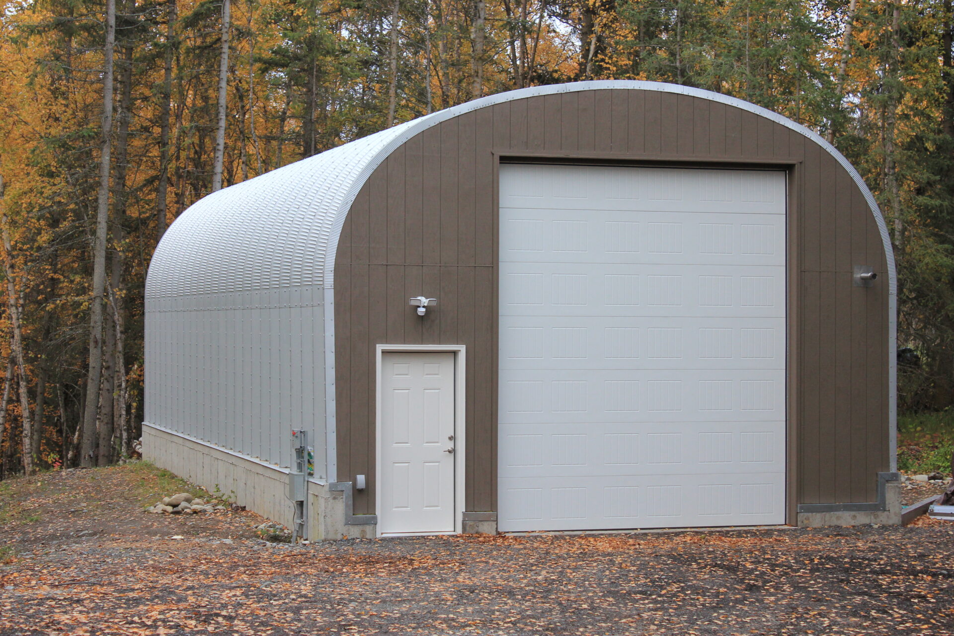 white quonset hut on concrete stem wall with brown custom endwall, white garage door and white entry door