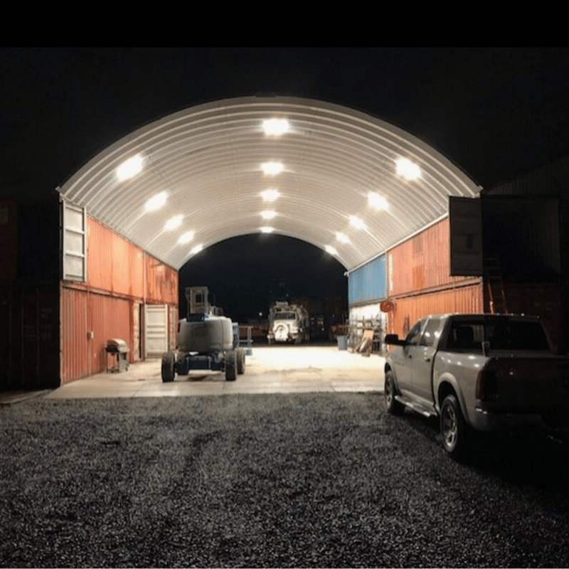 Night photo of shipping container storage set on stacked freight containers, arch lights illuminating the storage area sheltering various equipment.