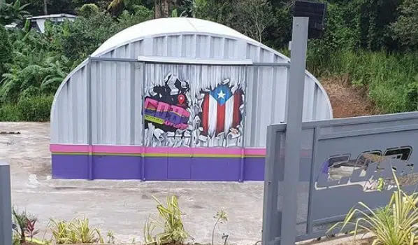 Personalized Quonset auto shop in Puerto Rico, steel endwall, painted front, purple, pink, and green striped base.