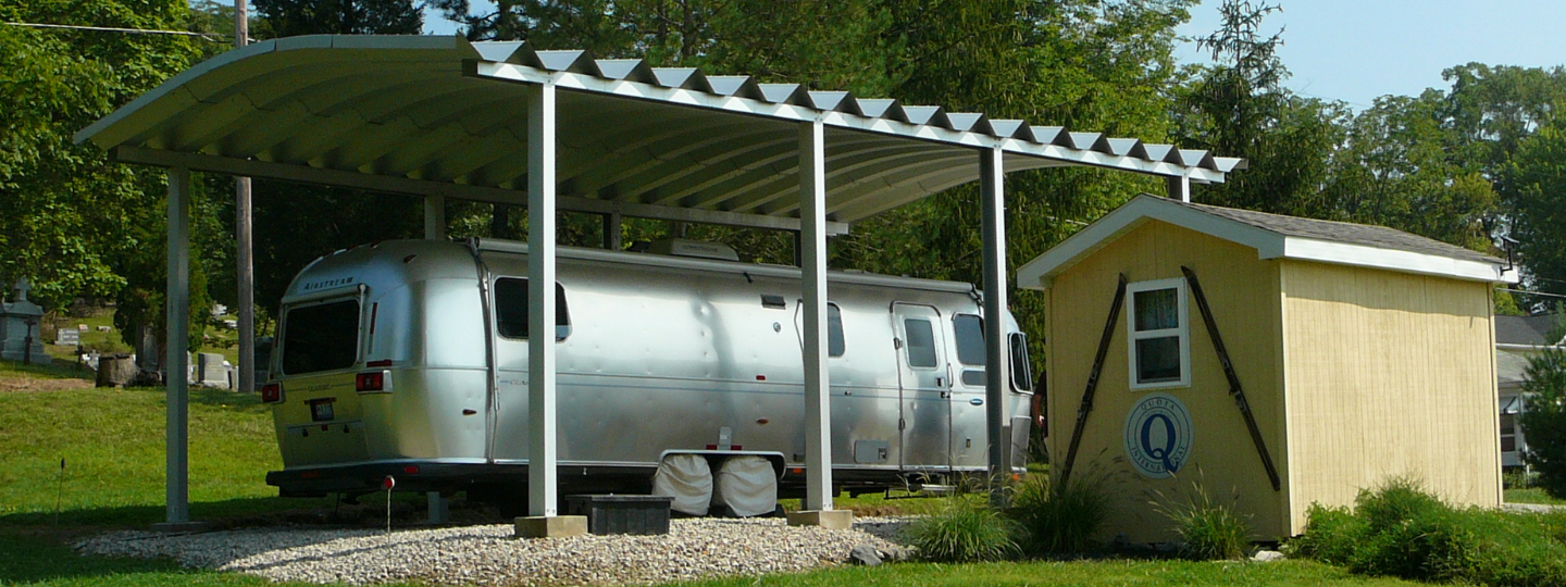 Steel RV in inside C-Model Carport with yellow shed in front